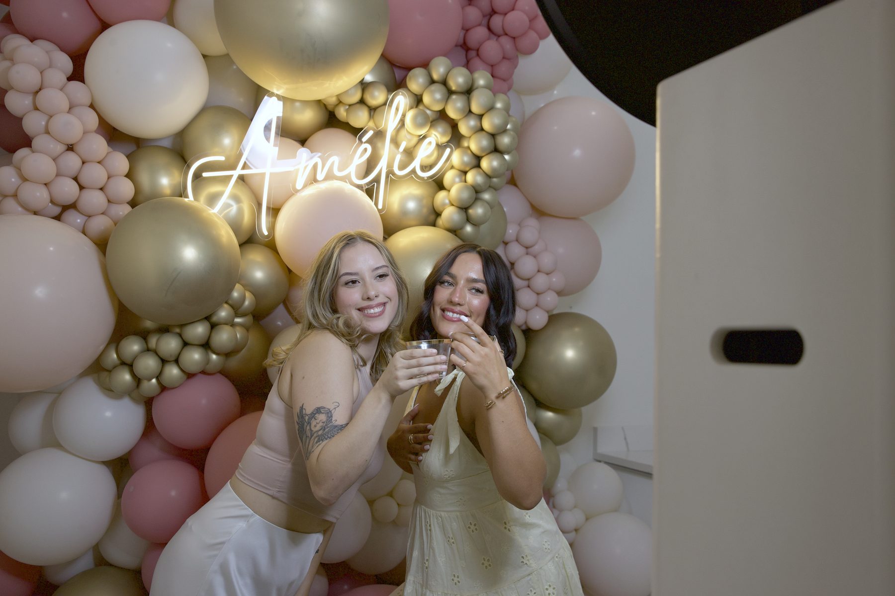 Two guests laughing in front of a balloon wall beside the EVNT Booth print photo booth
