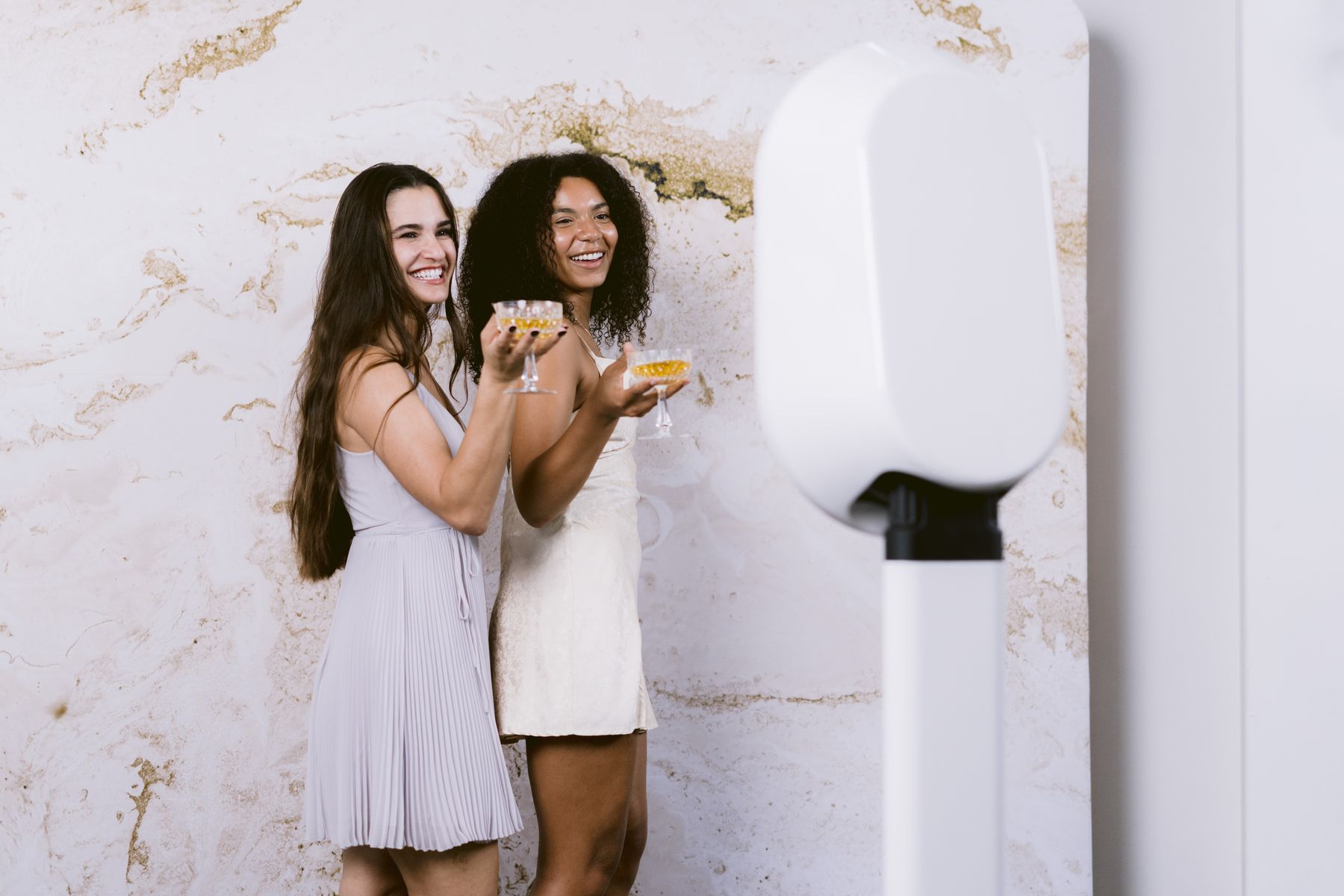 Guests posing with drinks next to the sleek white digital photo booth